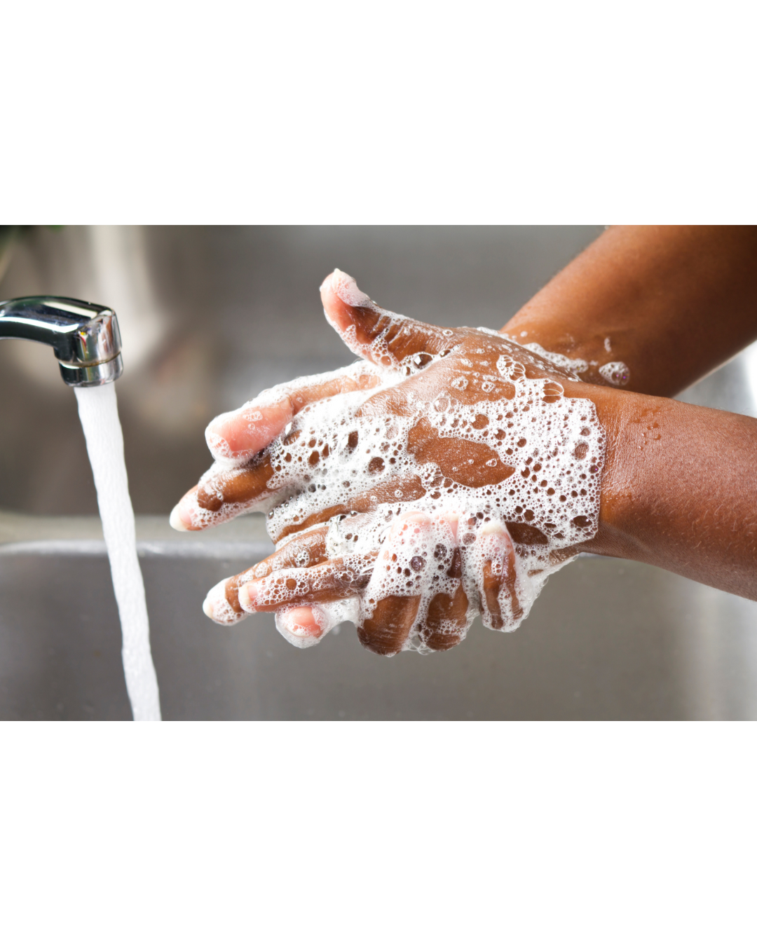 A person washing their hands next to a running faucet.